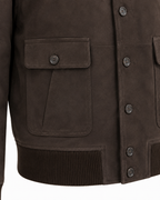Close-up of a dark brown suede jacket featuring a buttoned chest pocket, ribbed knit hem, and matching dark buttons on the front closure.
